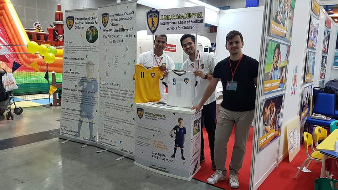 Academy representatives displaying football shirts at the Junior Academy booth at the KLCC Education Fair.
