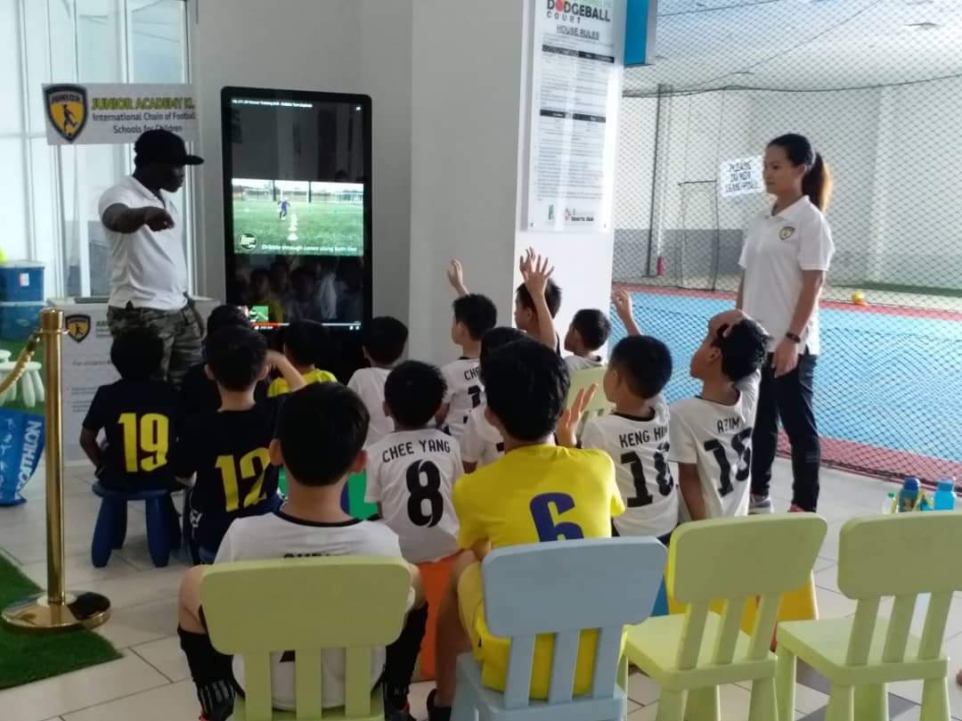 Young players raising their hands during a football learning session led by academy coaches.