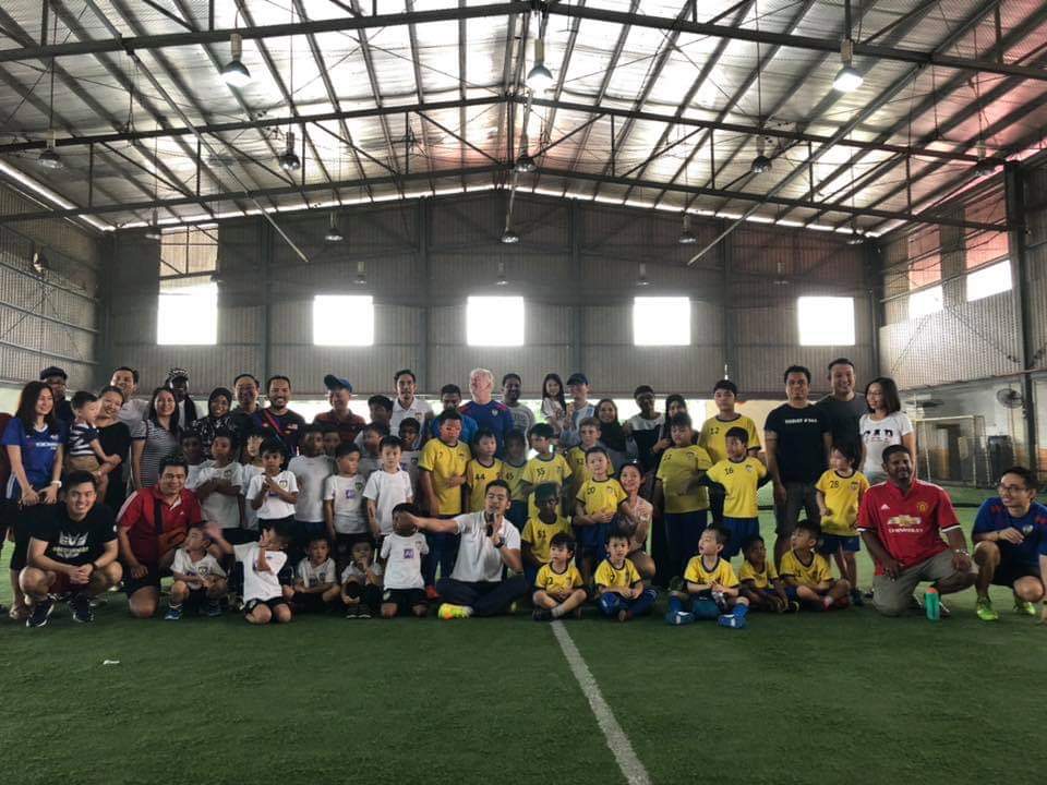 Players, coaches and families gathered for a group photo on an indoor football pitch.