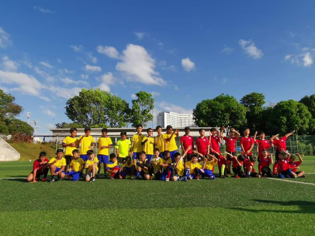 Young footballers in yellow and red kits posing together on an outdoor pitch.