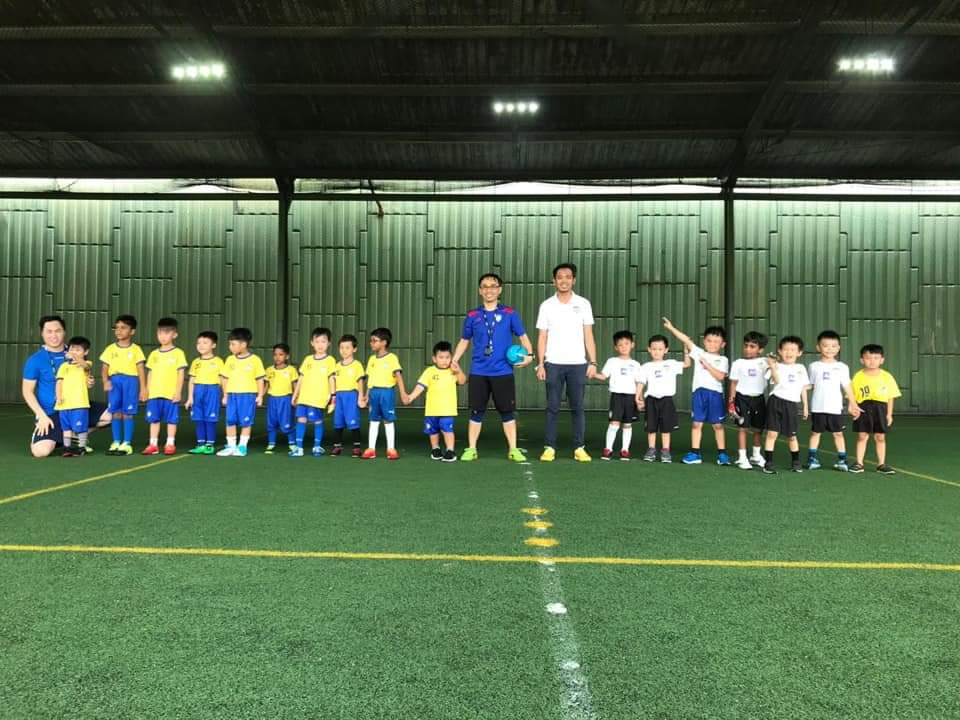Two teams of young footballers and their coaches lined up across an indoor pitch.
